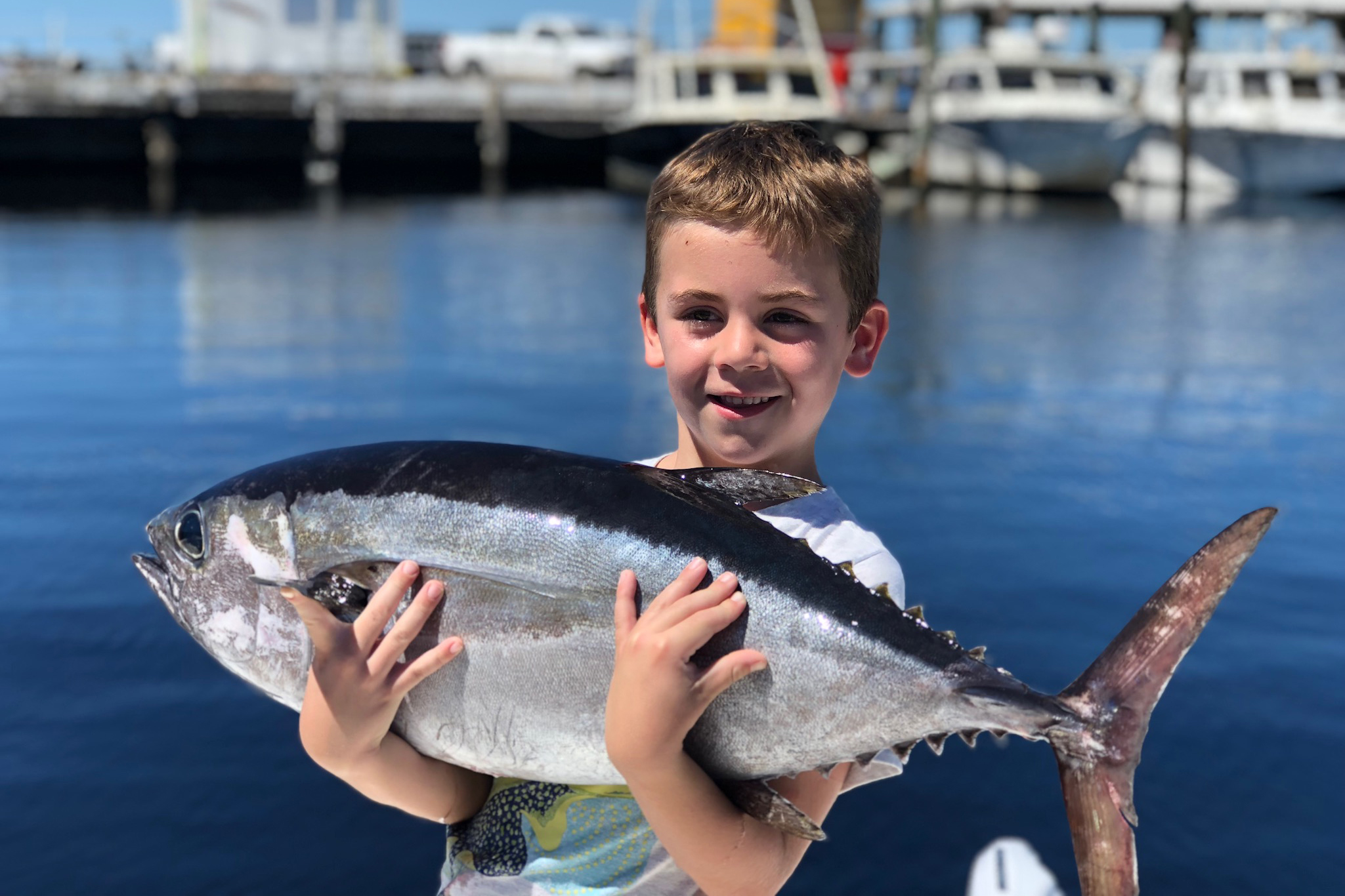 Ein lächelndes Kind mit einem Thunfisch, den er auf einer Angeltour gefangen hat