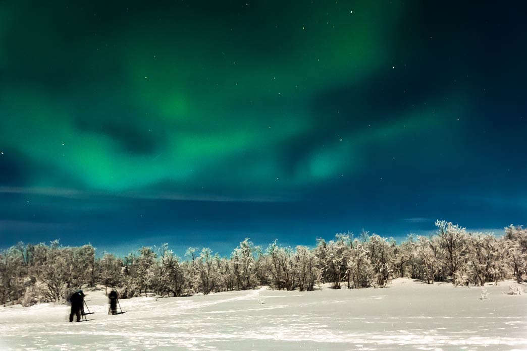 Drei Personen gehen auf der schneebedeckten Oberfläche unter dem Nordlicht am Polarkreis, Abisko, Schweden