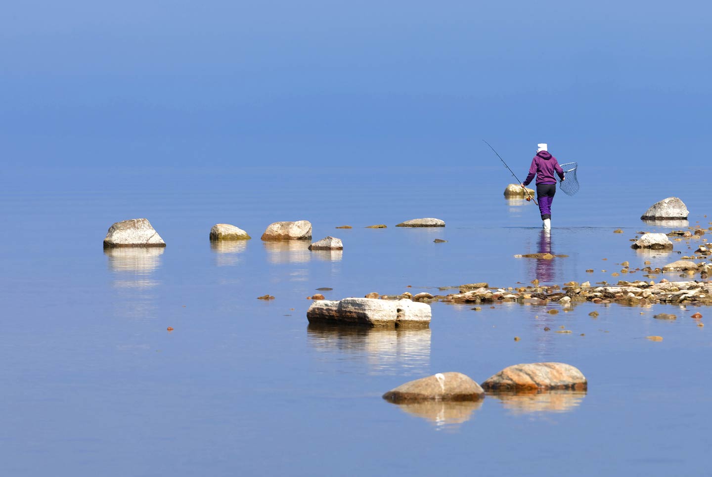 Eine Anglerin geht am ruhigen Wasser der Ostsee spazieren