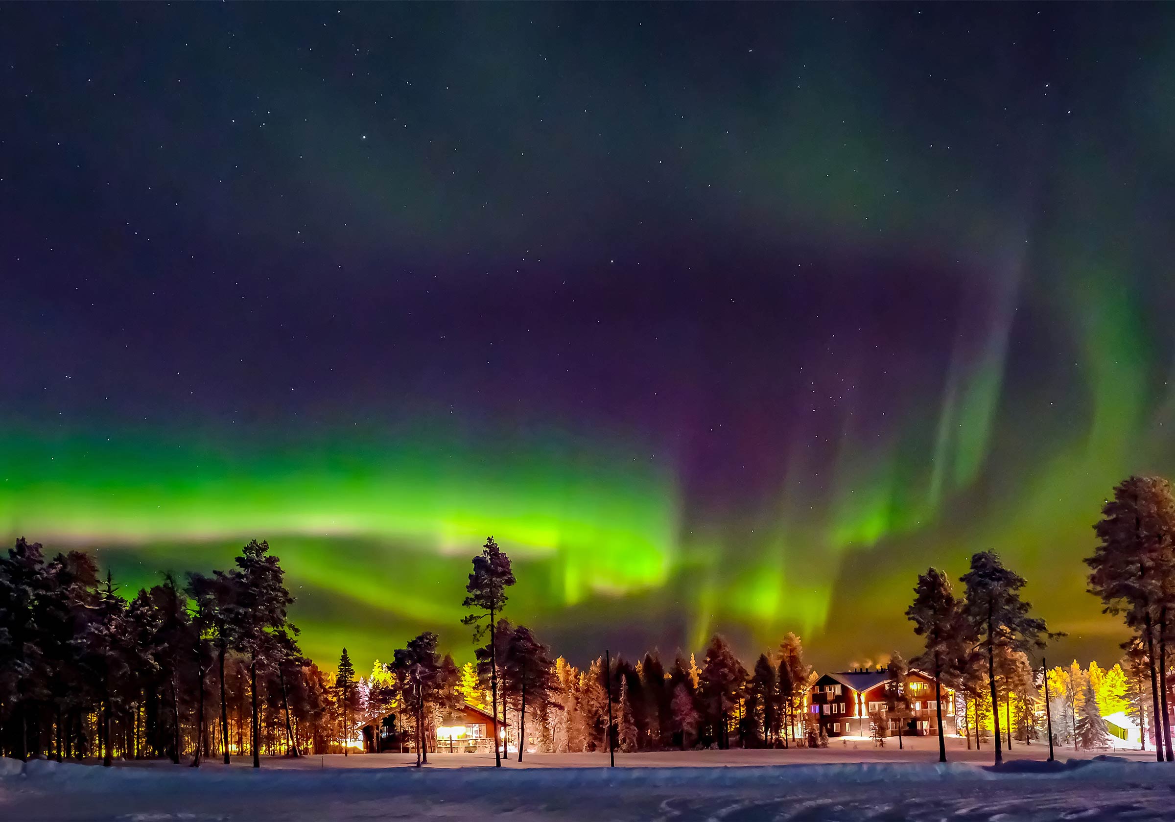 Nordlichter mit einer Stadt in der Ferne in Lappland, Finnland