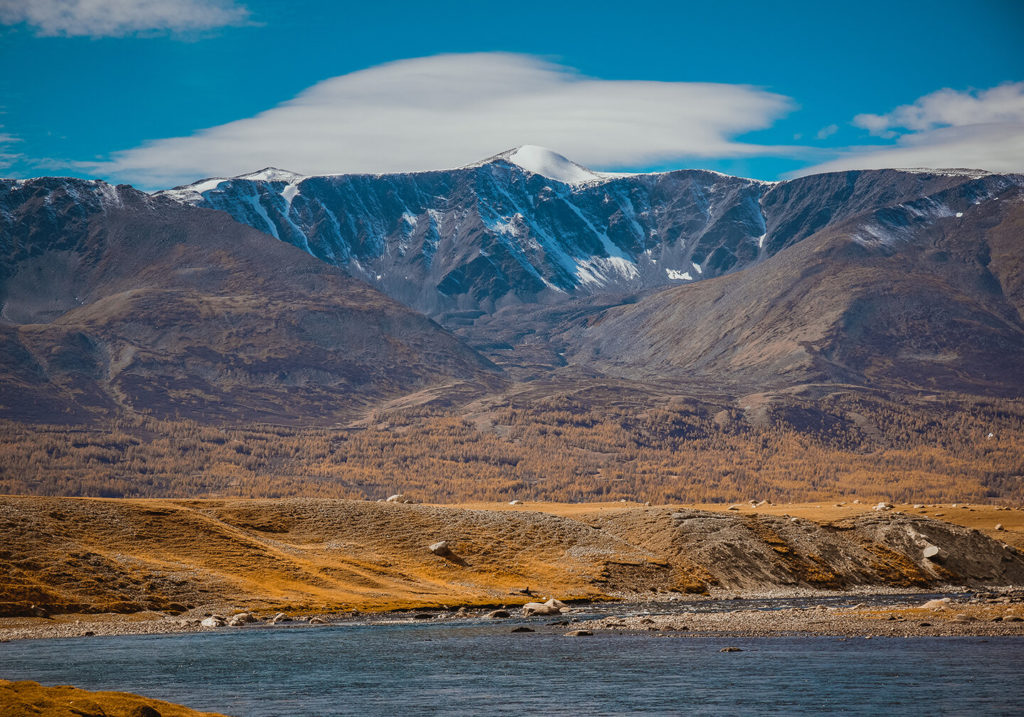 Ein Blick auf das mongolische Hochland mit Wasser im Vordergrund und schneebedeckten Bergen in der Ferne.