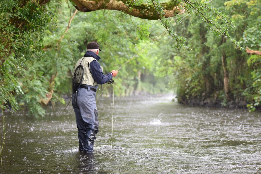 Ein Angler fischt mit der Fliegenrute in einem Fluss, während es regnet.