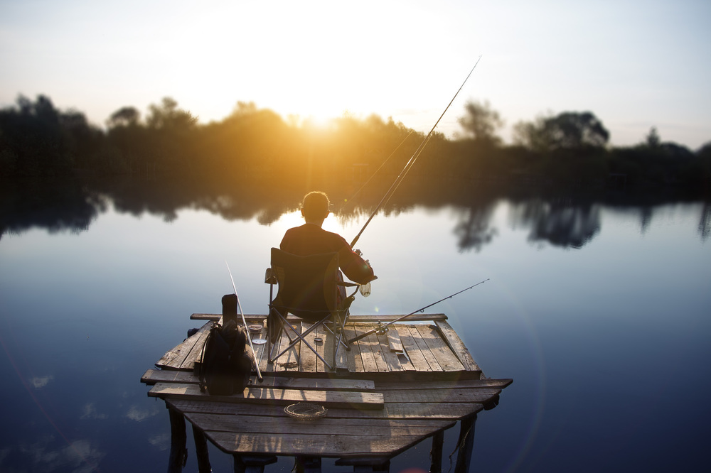 Ein Angler, der im Morgengrauen von einer kleinen Holzplattform aus angelt.
